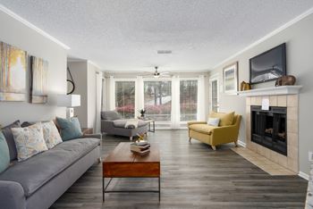A living room with wood-look flooring, a tile-surround fireplace, and floor-to-ceiling windows.